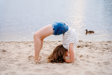 Young teenager girls makes a bridge acrobatic gymnastics girls on the beach. A young woman...