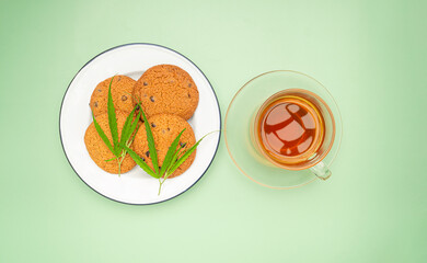 Cannabis chocolate chip cookies on a white plate and a glass of cannabis tea over a green background