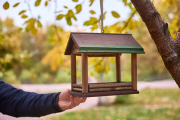 brown bird feeder hanging on tree branch with yellow leaves, autumn landscape. selective focus, background blur