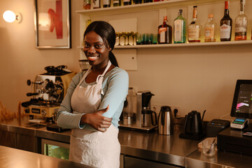 Young beautiful smiling african woman in apron with folded arms