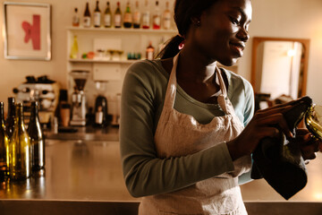 Young smiling african woman in apron rubbing glass closeup