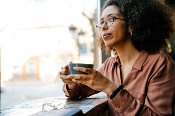 Young black woman smiling and drinking coffee in cafe indoors