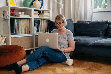 Obraz premium caucasian woman sits on floor in her living room and using laptop computer