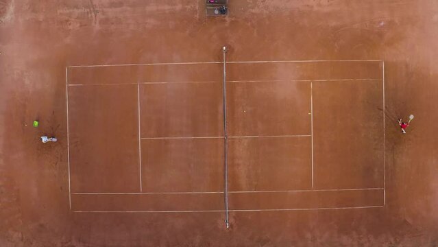 Players practicing tennis at clay court, hitting net, overhead shot.
