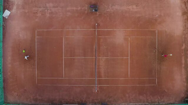 Tennis players at clay court, hitting net, zooming overhead shot.