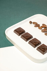 Handmade bitter chocolates on white plate with cocoa beans on green background.