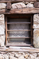 Old wooden window with wooden bars on a house made with stones