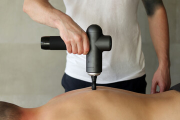 Sports percussion massage in medical room of gym. Masseur does massage exercises. Percussions therapy for regenerating massage of sport body. Concepts of rehabilitation of sports injuries.