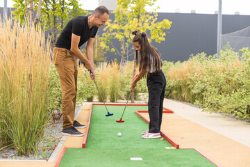 father and daughter playing mini golf - obrazy, fototapety, plakaty