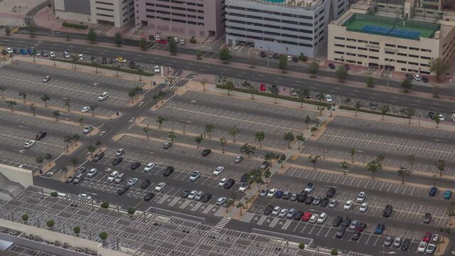 Big parking lot near mall crowded by many cars timelapse aerial view. Vehicles moves in and out during evening time
