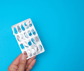 Woman's hand holding an empty blister pack on a blue background