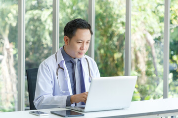 Fototapeta premium Portrait of asian senior doctor sitting in medical office while using laptop computer.