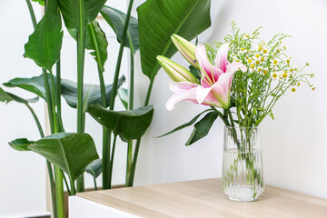 Beautiful bouquet of flowers (pink lilies along with small daisies) in glass vase on wooden surface besides a Giant White Bird of Paradise (Strelitzia nicolai), freshening and decorating home