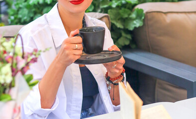 A girl in a white shirt with red lipstick holding a gray ceramic cup and saucer in her hand. Hot drinks. Herbal tea. Phytotherapy. Tea ceremony Concept.