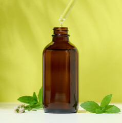 Brown glass bottle with a cosmetic product and a pipette with a drop, green background.