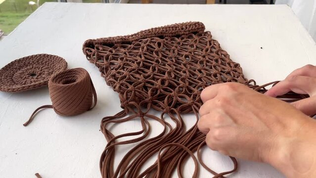 Close-up of women's hands weaving a string bag from a brown knitted cord in the macrame technique. Do it yourself.
