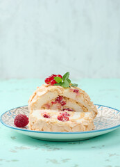 Baked meringue roll with red berries on a round plate, white background