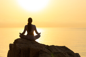 silhouette of young woman practice yoga and meditation near the sea at sunrise, healthy lifestyle concept, lotus position