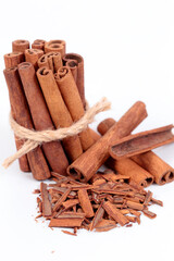 Group of cinnamon sticks on white surface, one in the foreground with ground cinnamon and one in the background. Selective focus.