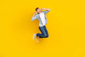 Full length photo of positive guy dressed blue shirt jeans sneakers jumping showing v-sign tongue...