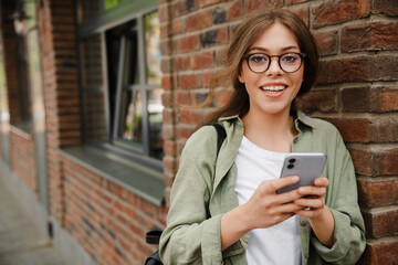 Young beautiful smiling woman in glasses looking camera holding phone