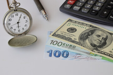 Banknotes spread out on a table with a calculator and a old watch