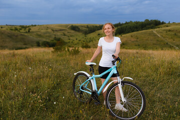 Young redhead woman with a bicycle in the field