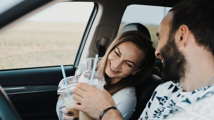 Caucasian cheerful woman sitting inside car and drinking coffee with her boyfriend, happy middle-aged couple on road trip