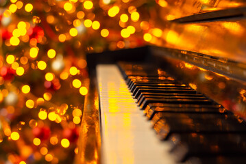 Close up photo of piano with bright decorated Christmas tree on the background. Celebrating Christmas with live music in cozy interior