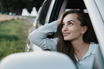 Cheeful caucasian woman with braces enjoying road trip and looking out from car window - obrazy, fototapety, plakaty