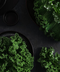 Green kale cabbage leaves on dark backgtound. Textured leaves in  black plate. Top view closeup....