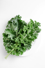 Fototapeta premium Green kale cabbage leaves on white background. Textured leaves in white plate. Top view and copyspace. Healthy food concept.