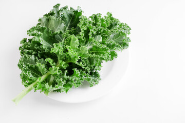 Green kale cabbage leaves on white background. Textured leaves in white plate. Top view and copyspace. Healthy food concept.