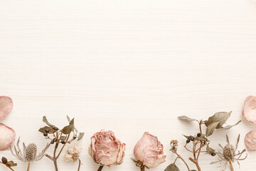 Decorative frame with dried pink roses on a light wood-grain background