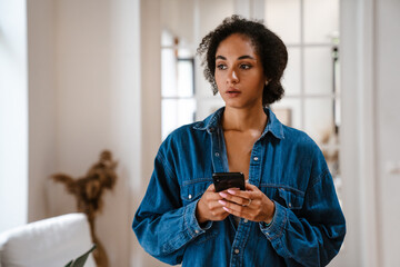 Young black woman wearing denim shirt using cellphone at home