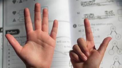 Closeup shot of a child counting with their fingers and doing their maths homework
