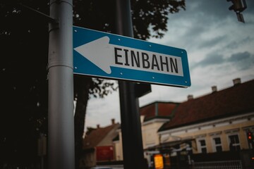 Closeup shot of a blue one-way road sign with an arrow and a blurred background of buildings