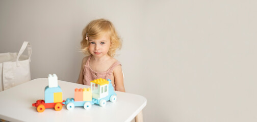 Pretty caucasian 1,2 year old with blond curly hair playing with colourful construction, erector set, toys making train.Nursery, preschool concept.Copy space.