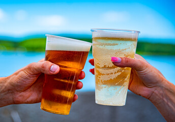 two plastick cup of beer in man and woman hands. Beer clinking outdoor