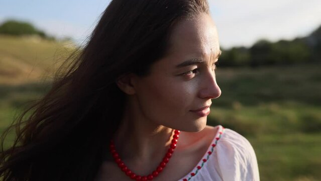 Portrait of young Ukrainian woman looking at side in traditional national embroidered shirt and necklace on meadow.