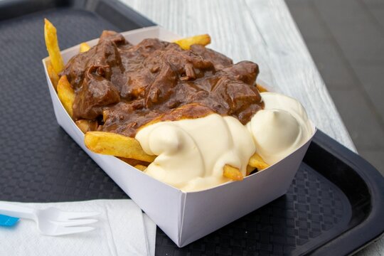 Closeup of a delicious Belgian beef stew on fries on a black plastic tray in a restaurant