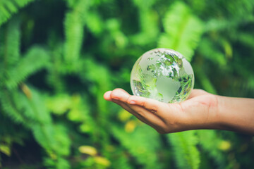 Human hands holding earth sphere crystal or sustainable globe glass with sunlight at green nature...
