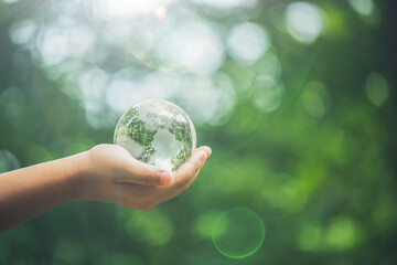 Human hands holding earth sphere crystal or sustainable globe glass with sunlight at green nature...