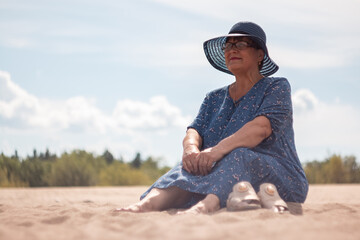 Fototapeta na wymiar An elderly woman goes sitting on the sandy shore.