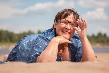 An elderly woman lies on a sandy shore.