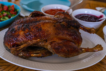 Roasted whole Peking duck with apples and sauces in gravy boats. Traditional holiday dish. Fried crust with honey. High quality. Homemade holiday dinner.