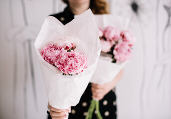 Very nice young woman's hand holding big and beautiful bouquet of fresh white and pink peony flowers, wrapped i pink paper on the pink background, bouquet close up - 524072642