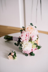 Beautiful bridal flower wedding bouquet of fresh roses, peonies, eucalyptus flowers in tender pink colors with a small matching boutonniere, close up view