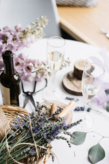 Two glasses of white wine, wine bottle, with delphinium flowers on the white table on the background