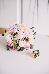 Beautiful bridal flower wedding bouquet of fresh roses, peonies, eucalyptus flowers in tender pink colors with a small matching boutonniere, close up view